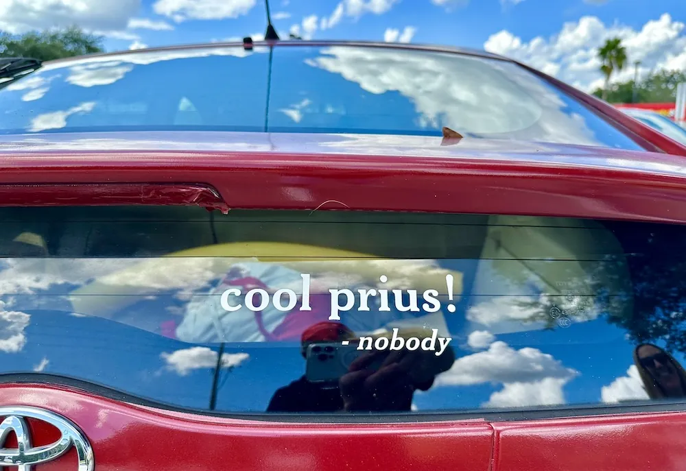 Photo of the back of a Prius, with a writting in it in white that reads: &ldquo;Cool Prius! - nobody&rdquo;